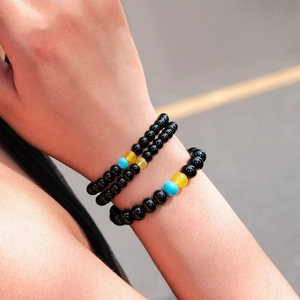 Detail of stacked black onyx beaded bracelets with sky blue and lemon yellow accents