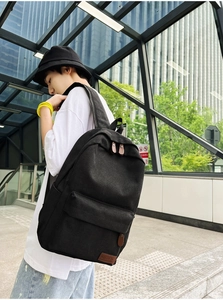 Detail view of black canvas backpack with brown leather patch and side pocket straps
