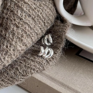 Macro shot of chunky silver multi-layer hoop earrings on a warm textured knit background
