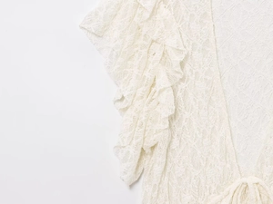 Détail de haut en dentelle blanche avec broderie florale ajourée et bordures à volants