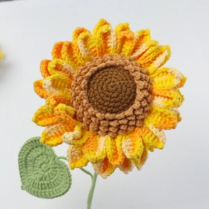 Close-up of handmade crochet sunflower with yellow-orange petals and green leaf