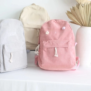 Detailed view of personalized corduroy backpacks in pink, grey, and beige with flower embroidery
