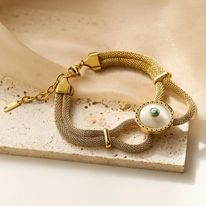 Gold multi-strand mesh chain bracelet with white disc and teal bead on beige stone