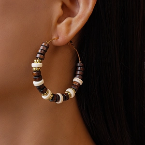 Détail de boucles d'oreilles créoles avec perles en bois marron et nacre sur modèle
