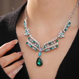 Macro shot of silver wing and flower necklace with teardrop green gemstone pendant