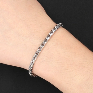 Detailed close-up of a silver-toned chunky Cuban chain bracelet with a woven metal texture
