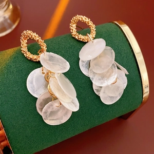 Elegant gold round earrings with layered shell tassels on a velvet jewelry display