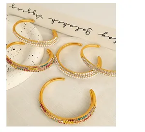 Close-up of gold-plated open bracelets with layered pearls and colorful crystals
