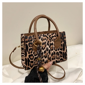 Detailed view of leopard print handbag with brown handles and a woven charm ornament