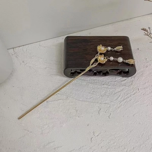 Detail of golden magnolia hairpin with pearls and delicate tassel on a wooden base