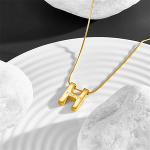 Detail view of gold titanium sweater necklace featuring an H pendant with Fashion engraving
