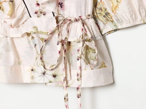 Detail of floral linen blend top featuring adjustable waist tie and ruffled hem design