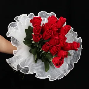 Red rose bouquet wrapped in layered white pleated lace with pearl edge and green leaves