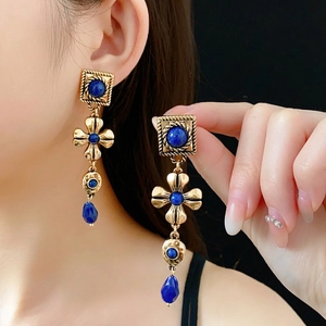 Vintage gold dangling earrings with blue stones and tassel design in a hand-held view
