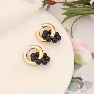 Detail of golden hoop earrings with black beads on a white ceramic plate and floral backdrop