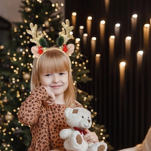 Child wearing golden glitter reindeer antler headband with bells and berries for Christmas