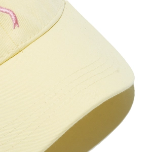 Detail of light yellow baseball cap featuring twill cotton texture and pink embroidery