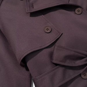 Gros plan sur les boutons croisés et la texture épaisse du tissu du trench-coat violet