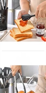 Action shot of black silicone spatula spreading jam and food tongs holding bread slice