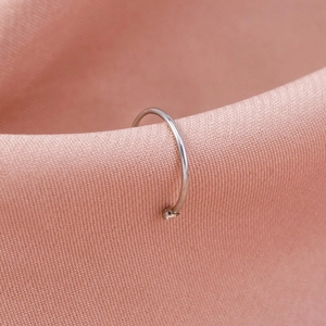 Detailed close-up of a polished silver stainless steel U-shaped nose ring on pink fabric