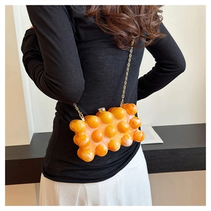 Détail de la pochette en acrylique orange avec chaîne dorée portée à l'épaule