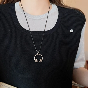 Detail of creative silver headphone pendant on black cord worn over a knit sweater