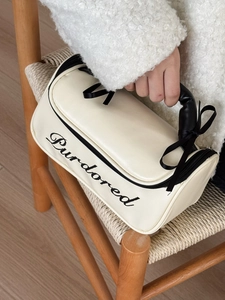 Close-up of cream cosmetic bag with black embroidery and ribbon bow on a woven chair