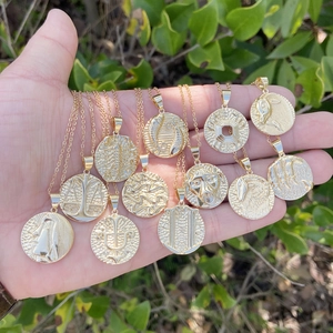 Hand holding twelve 18K gold zodiac pendants on chain necklaces with embossed patterns