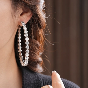Close-up of a model wearing large silver hoop earrings with sparkling crystal rhinestones
