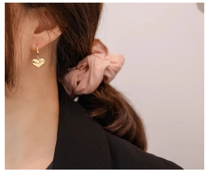 Close-up of a model wearing polished gold heart-shaped earrings with a metallic finish