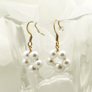 Elegant gold hoop earrings with white pearls hanging on a glass with white veil