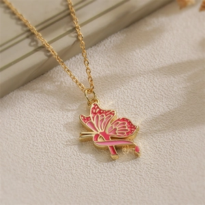 Golden butterfly necklace with pink enamel pendant on a soft beige textured surface