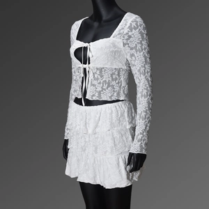 Detail of floral lace texture on white long sleeve crop top and layered skirt set