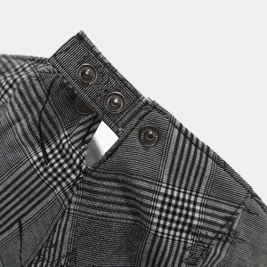 Close-up of black and white plaid fabric featuring three industrial metal snap buttons