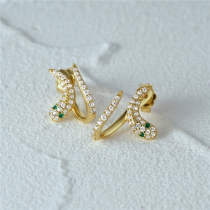 Macro detail of gold snake earrings with white pavé zircons and green gemstone eyes