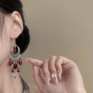 Close-up of bohemian earrings featuring red beads and silver leaf charms on a model