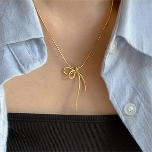 Detail of golden bow pendant necklace on a model featuring a fine snake chain