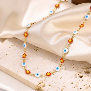 Detail of gold daisy and evil eye necklace on beige silk and stone background