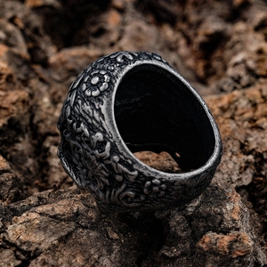 Vintage stainless steel skull ring with embossed floral patterns on rustic bark background