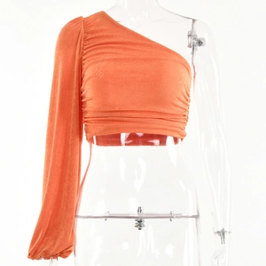 Détail du crop top orange à une épaule et manches longues avec texture plissée élégante