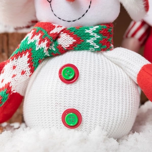 Plush Christmas snowman doll with red and green knit scarf on a snowy wooden background