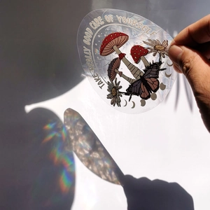 Suncatcher window sticker with mushroom and butterfly casting rainbow light on hand