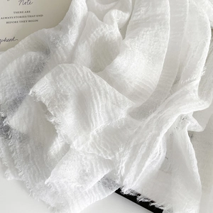 Detailed texture of a white linen scarf with frayed edges and pleated lightweight fabric