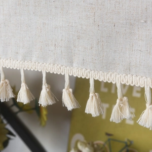 Detail of beige linen curtain fabric with elegant fringe tassels and rustic texture