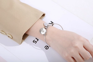 Détail de pendentifs cœur et cercle argentés avec gravure 'mi mama' sur un bracelet