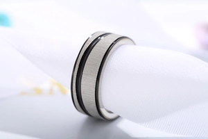 Close-up of brushed stainless steel ring with black parallel grooves on white silk