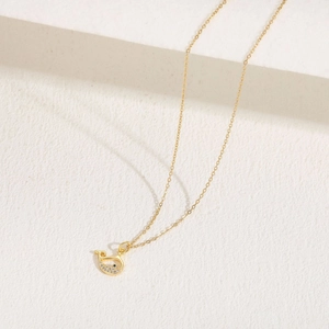 Detailed view of a 14K gold-plated whale pendant with blue gemstone and zircon on beige fabric
