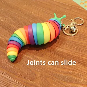 Rainbow sensory slug keychain with movable joints and golden bell on dark wood