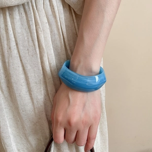 Detailed view of wide light blue marbled acrylic cuff bracelet worn with pleated skirt