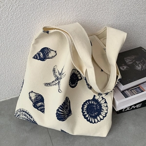 Detail of off-white canvas tote bag featuring navy blue hand-drawn sea shell patterns